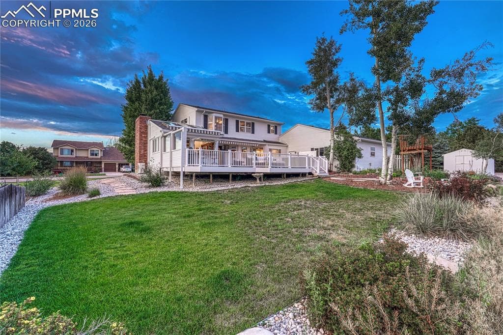 Expansive backyard with a manicured lawn, a multi-level deck, mature trees, and a storage shed