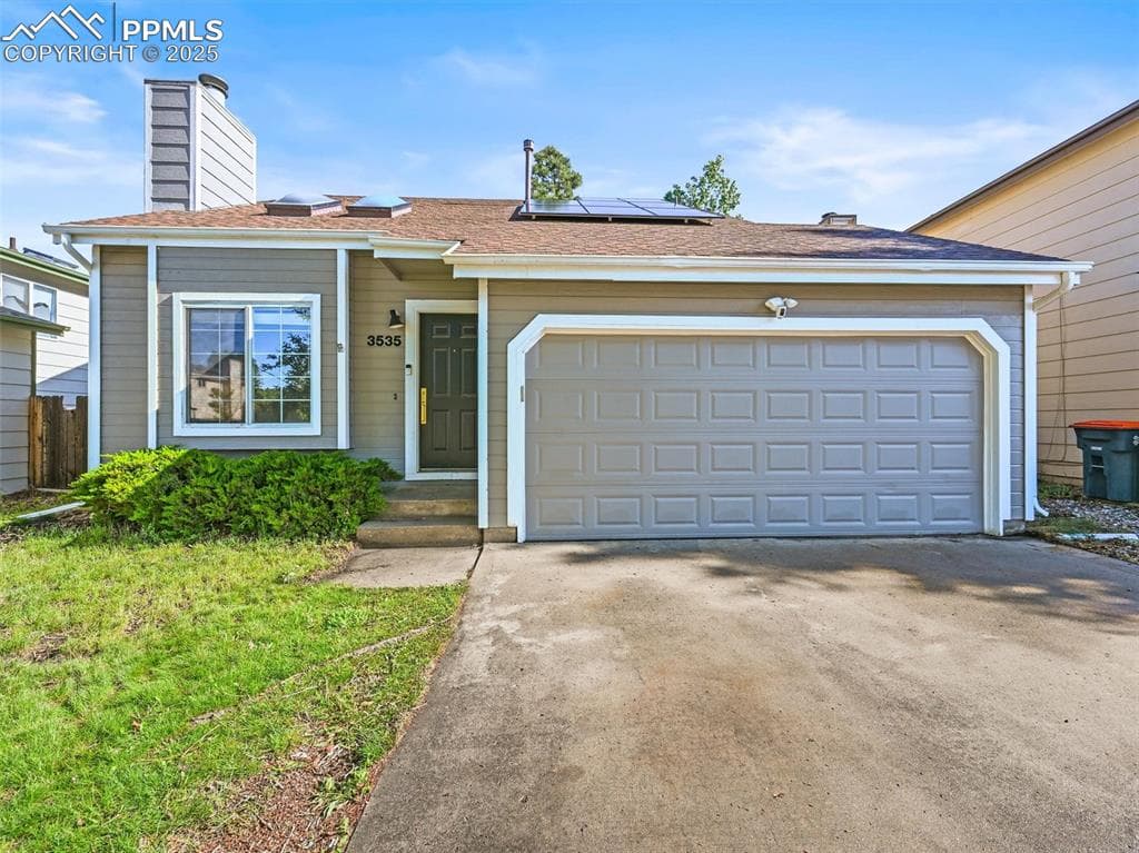 View of front of house with a chimney, solar panels, concrete driveway, and an attached garage