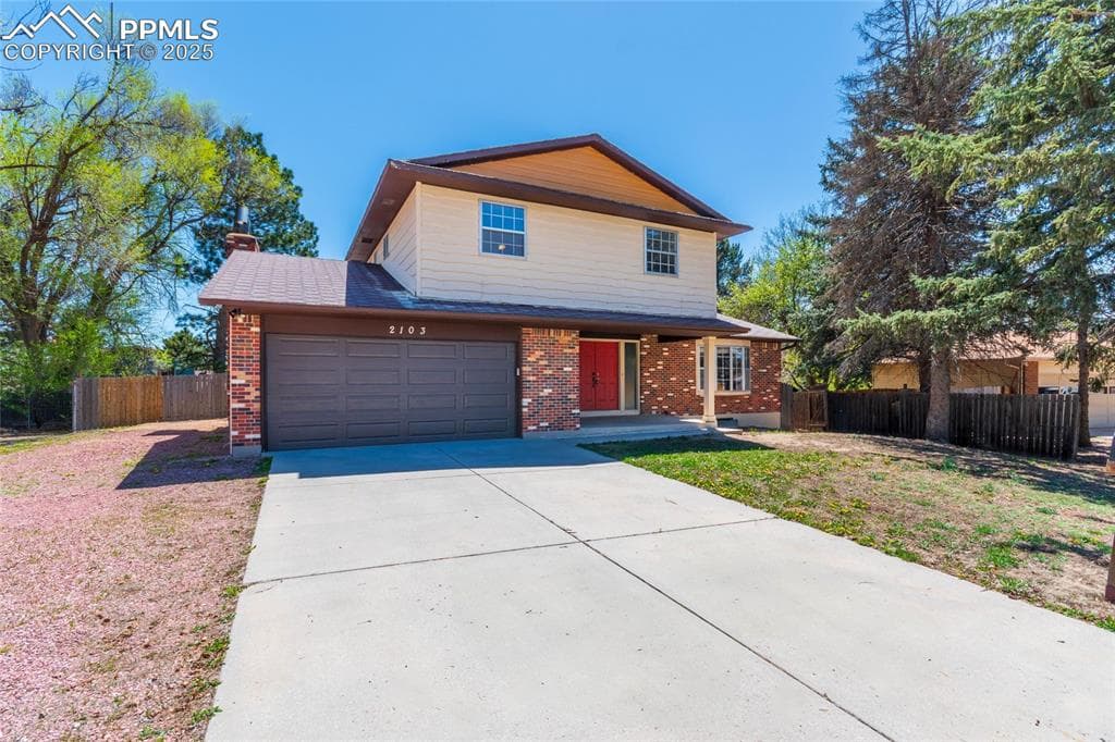 Traditional-style house with fence, an attached garage, brick siding, and concrete driveway