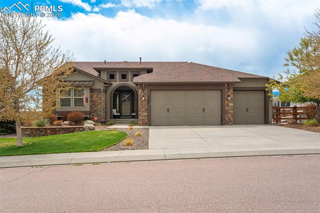 Stucco and stone facade with a prominent arched entry, dual garage doors, a concrete driveway, and mature landscaping