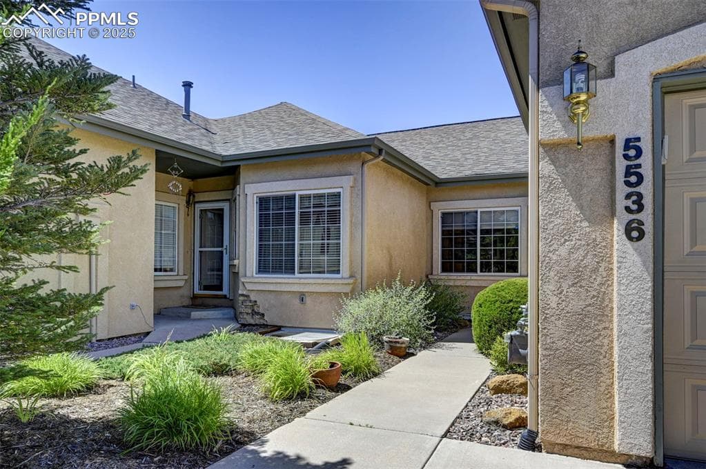Property entrance featuring roof with shingles and stucco siding