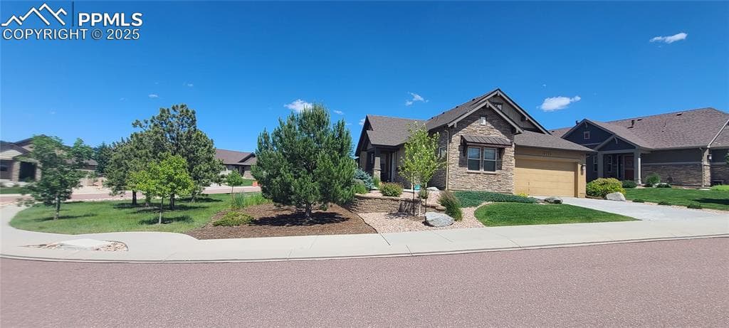 Craftsman-style home with stone siding, a garage, concrete driveway, and a front yard